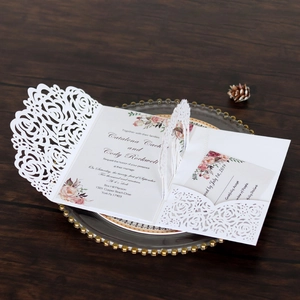Detail of white laser-cut wedding invitation with rose hollow design and floral inserts