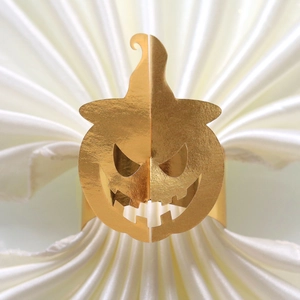Detailed view of golden Halloween pumpkin napkin ring with cutout design on white fabric