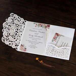 Detailed laser cut white floral wedding invitation set with RSVP card on wooden background