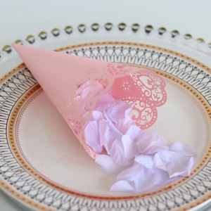 Detail of pink laser-cut lace wedding paper cone with purple flower petals on a plate