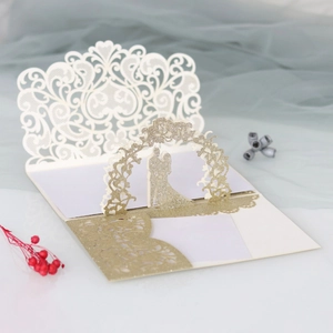 Detail of laser-cut wedding card with couple under floral arch and gold glitter inner