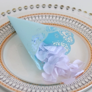 Laser-cut light blue paper cone with lace edge and lavender petals on a plate