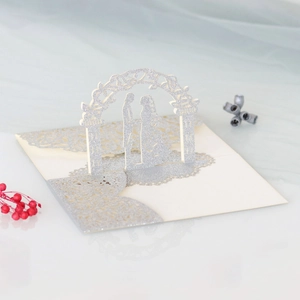 Detail of silver laser-cut 3D wedding card with bride and groom under a floral arch