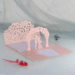 Macro view of 3D laser-cut pink wedding invitation showing intricate rose gate and couple silhouette