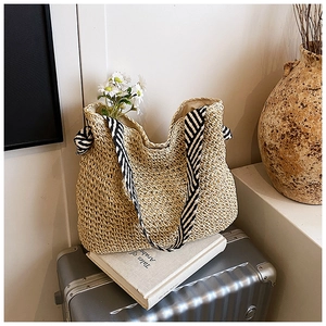 Détail d'un sac cabas en paille tissée avec bandoulières rayées noires et blanches sur valise