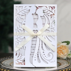 Detail of laser-cut wedding invitation featuring a couple silhouette and satin ribbon bow