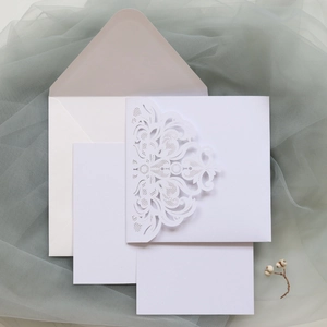 Macro view of laser cut lace wedding invitation with floral patterns and matching envelope