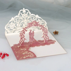 Macro detail of 3D pop-up wedding invitation with laser-cut lace and pink glitter silhouette