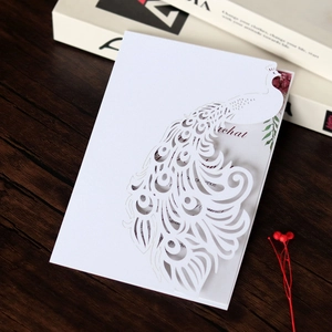Close-up of laser-cut peacock wedding invitation with intricate hollow details and inner page
