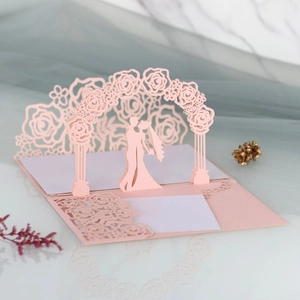 Macro view of laser-cut 3D wedding card with pink rose arch and romantic couple silhouette