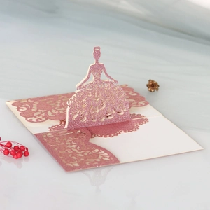 Detailed view of laser-cut 3D pop-up dress pattern on pink glitter wedding card