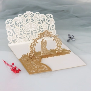 Detail of laser-cut wedding invitation featuring golden glitter 3D floral arch and couple