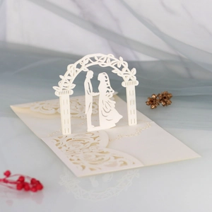 Macro view of white laser-cut 3D wedding invitation with lace arch and couple silhouette