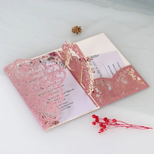 Close-up of laser-cut glitter wedding invitation with pink rose patterns and inserts