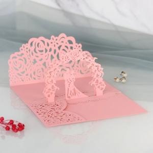 Dettaglio macro del biglietto di nozze 3D con arco floreale e silhouette sposi intagliata