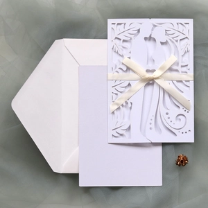 Detail of laser-cut white wedding invitation with couple silhouette and ribbon bow