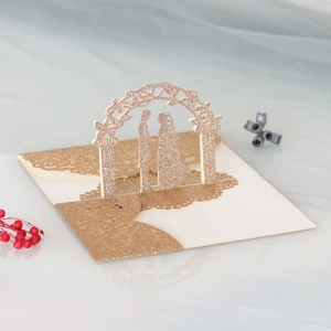 Close-up of laser-cut pop-up wedding card with glittery arch and couple silhouette