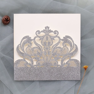 Close-up of laser-cut wedding invitation with silver glitter lace and floral patterns