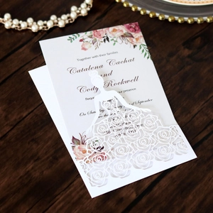 Detail of laser-cut floral lace wedding invitation with pink rose pattern on wood background