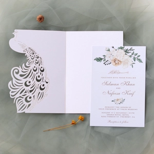 Detail showing white laser-cut peacock wedding invitation with floral printed insert card