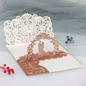 Detail of 3D laser-cut wedding invitation featuring rose gold glitter couple under a floral arch