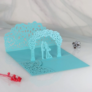 Macro view of blue laser-cut 3D wedding card with bride and groom under floral arch