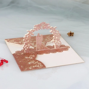 Macro detail of laser-cut 3D wedding card with rose gold glitter floral arch and lace