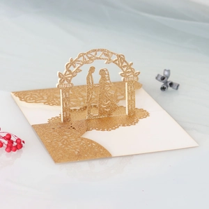 Detail of laser-cut gold glitter wedding card showing couple silhouette and floral hollows