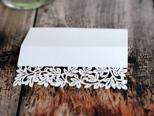 Close-up of white laser-cut leaf place card on rustic dark wood background for weddings