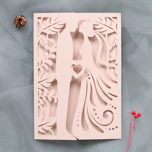 Close-up of laser-cut wedding invitation featuring bride and groom silhouette in blush pink