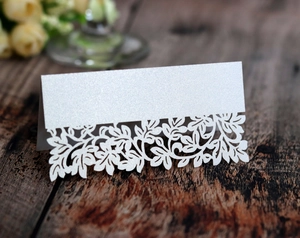 Macro detail of laser-cut white glitter table card with intricate hollow leaf patterns