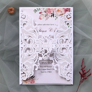 Detailed laser cut white lace wedding invitation with pink floral insert and ribbon