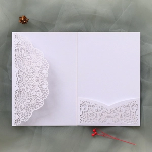 Detail of white laser-cut wedding invitation with intricate lace pattern on mesh background