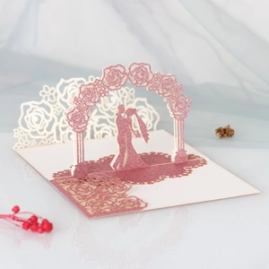 Macro detail of laser-cut 3D pop-up wedding card with pink glitter flower arch and couple