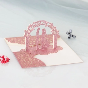 Detail showing pink glitter 3D laser-cut wedding card with couple under a rose archway