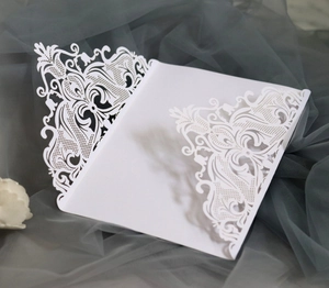 Close-up of white laser-cut wedding invitation featuring intricate floral lace patterns