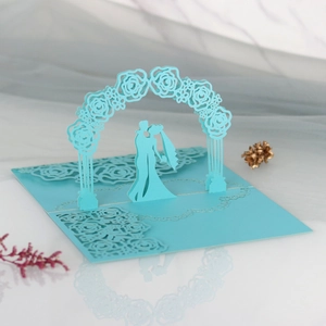 Macro detail of laser-cut 3D wedding card showing a couple kissing under a blue rose arch