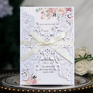 Close-up of laser-cut wedding invitation with cream ribbon bow and floral inner card