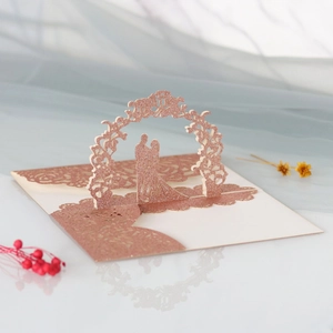 Détail d'une carte de mariage rose doré pailleté avec arche florale et silhouette de couple