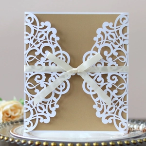 Intricate laser-cut floral wedding invitation with cream ribbon and elegant golden base card