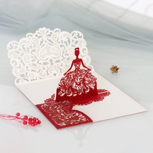 Macro shot of laser-cut 3D pop-up card featuring a red gown silhouette with gold glitter