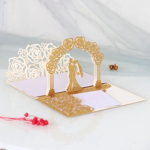 Macro view of a 3D pop-up gold glitter wedding card featuring a laser-cut rose arch and couple