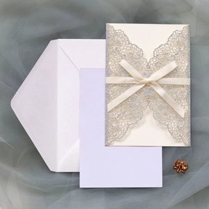 Flat lay of silver glitter laser-cut wedding invitation set with cream ribbon bow