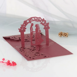 Macro detail of laser-cut burgundy 3D pop-up wedding card showing a couple under floral arch