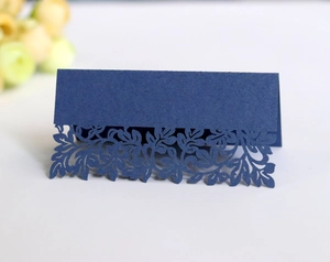 Macro detail of laser-cut leaf patterns on dark blue cardstock wedding place cards
