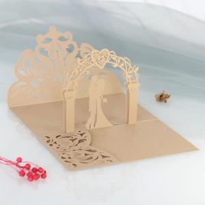 Detailed laser cut gold wedding invitation featuring a 3D pop-up arch and couple silhouette