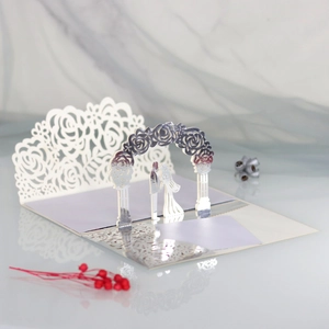Detail of 3D laser-cut wedding invitation featuring a kissing couple under a floral arch