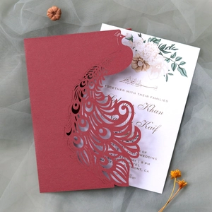 Macro detail of red laser-cut peacock wedding invitation with floral printed insert