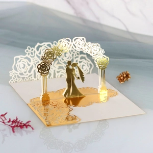 Detail of 3D laser-cut wedding invitation showing golden floral arch and kissing couple