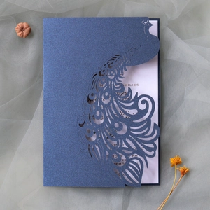 Detail of laser-cut peacock wedding invitation with dark blue glitter and elegant white insert